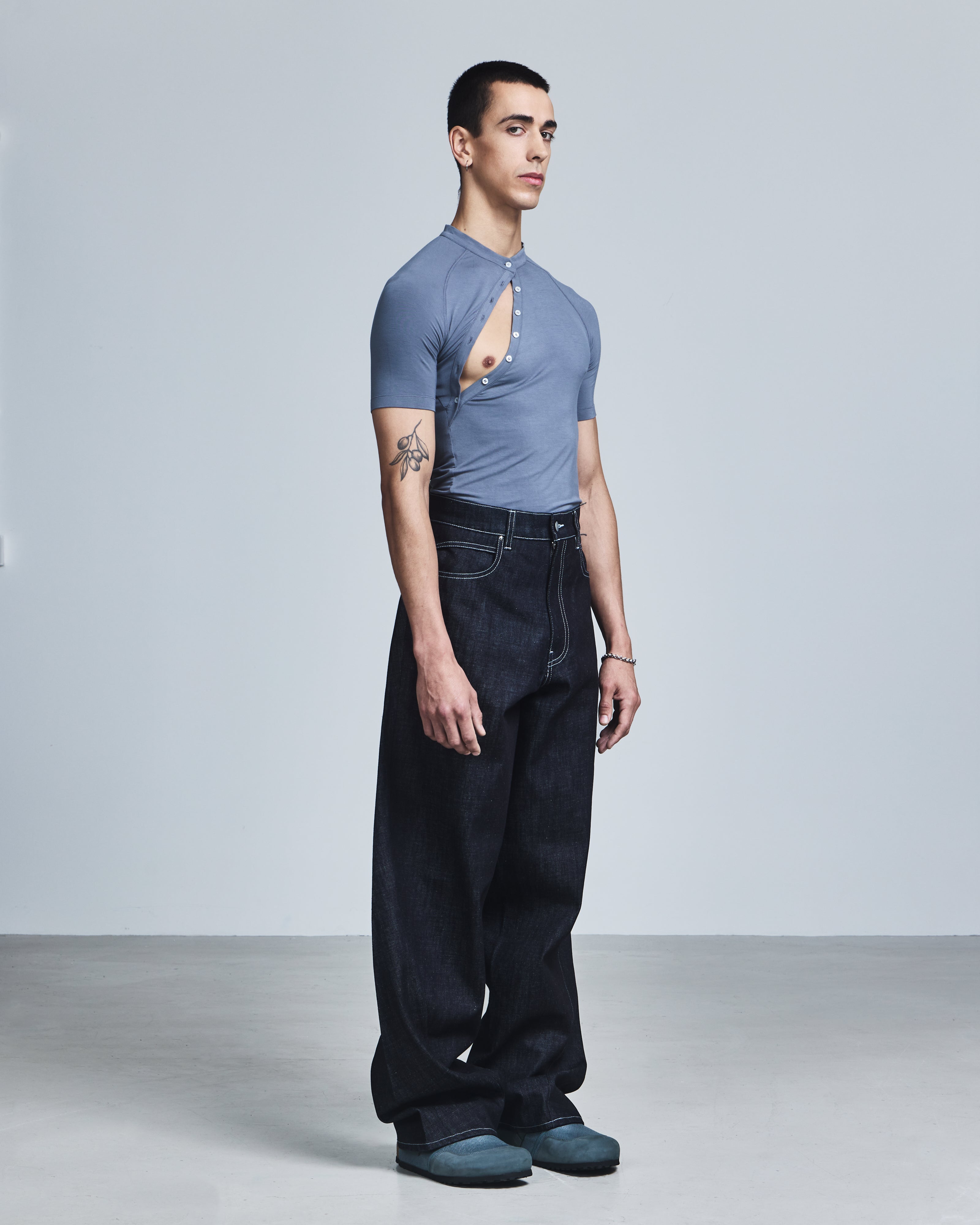 Man wearing a blue shirt with a cutout design and dark jeans on a plain background