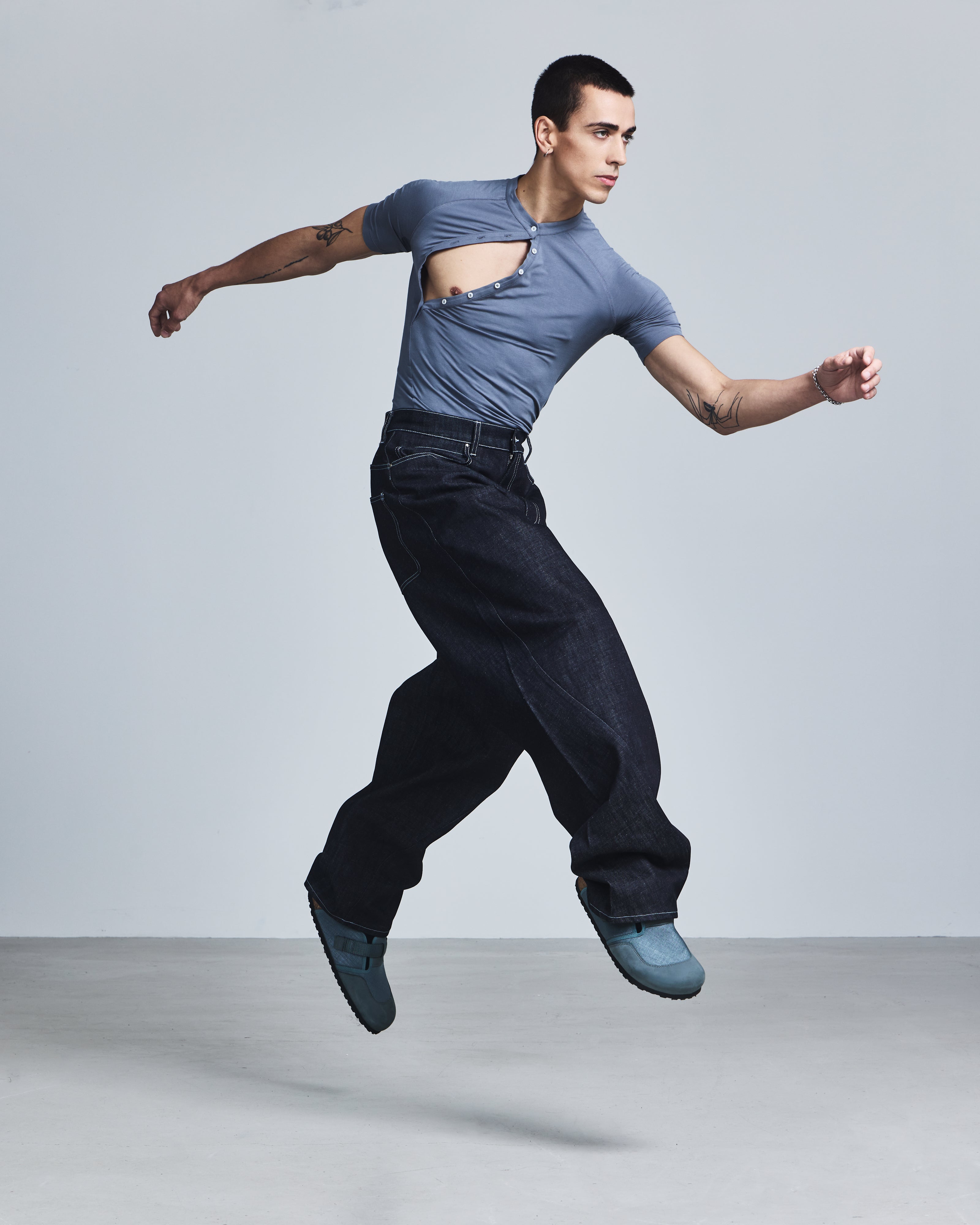 Man in a blue shirt and dark jeans jumping in a studio setting